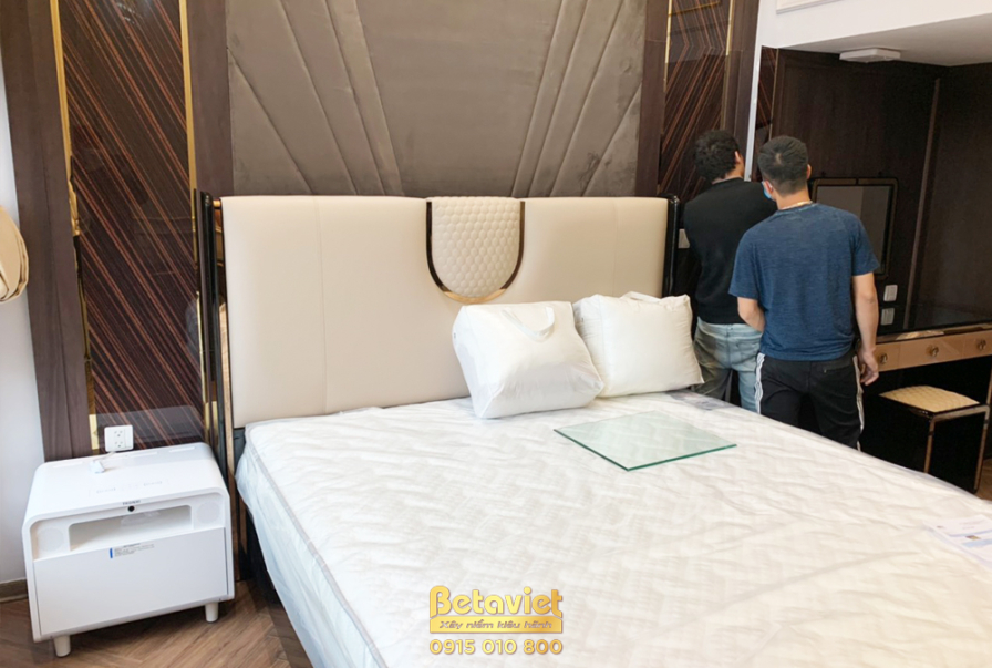 Không gian phòng ngủ đang trong giai đoạn lắp đặt hoàn thiện, tập trung vào giường ngủ bọc nệm màu kem sang trọng. Đầu giư…