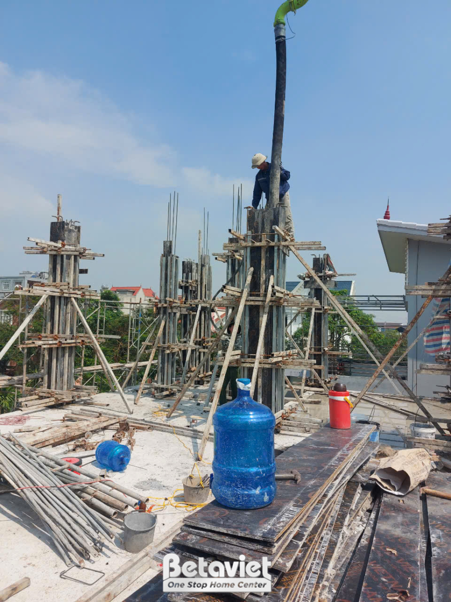 Công trường tầng thượng đang đổ cột bê tông cốt thép, giàn giáo thép cao bao quanh cụm cột, công nhân đứng trên cao thao t…