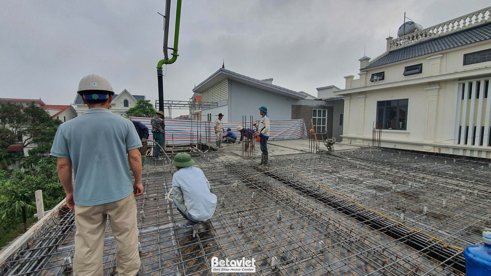 Công nhân đang thực hiện công việc đổ bê tông sàn mái của ngôi nhà phố. Máy bơm bê tông đang hoạt động, sắt thép đã được b…