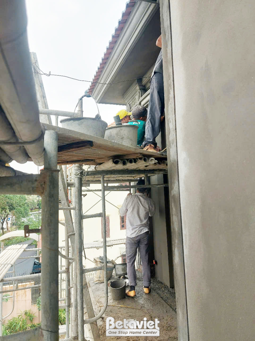 Công nhân đang thực hiện công việc trát tường hoặc hoàn thiện bề mặt ngoại thất của ngôi nhà phố. Giàn giáo được dựng chắc…