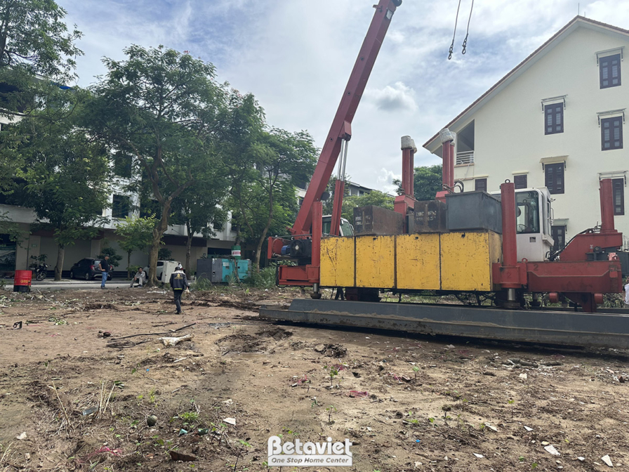 Máy móc hạng nặng đang hoạt động trên công trường, có cần cẩu lớn và các thiết bị phục vụ thi công móng. Nền đất trống với…
