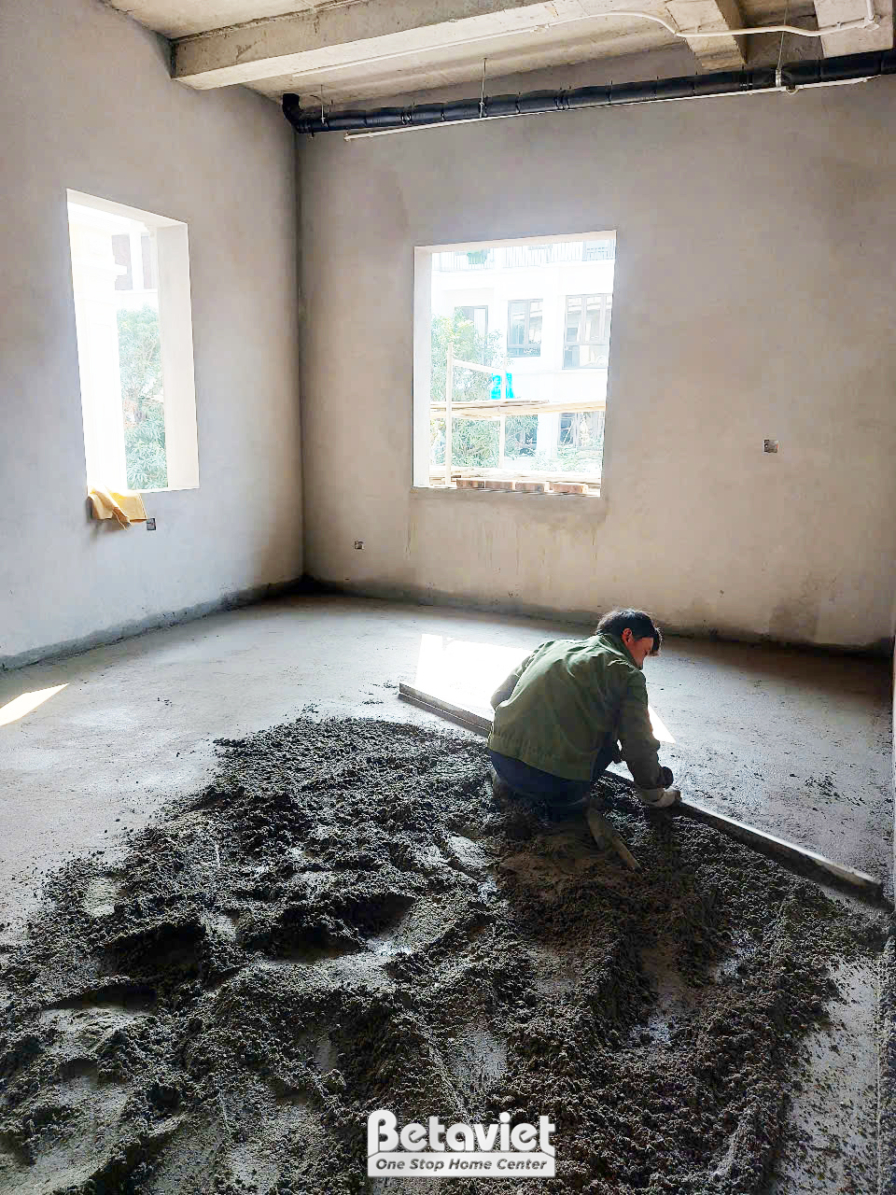Công nhân đang thực hiện công việc san lấp hoặc trát nền nhà bên trong ngôi nhà phố. Sàn nhà còn nguyên vật liệu xây dựng…