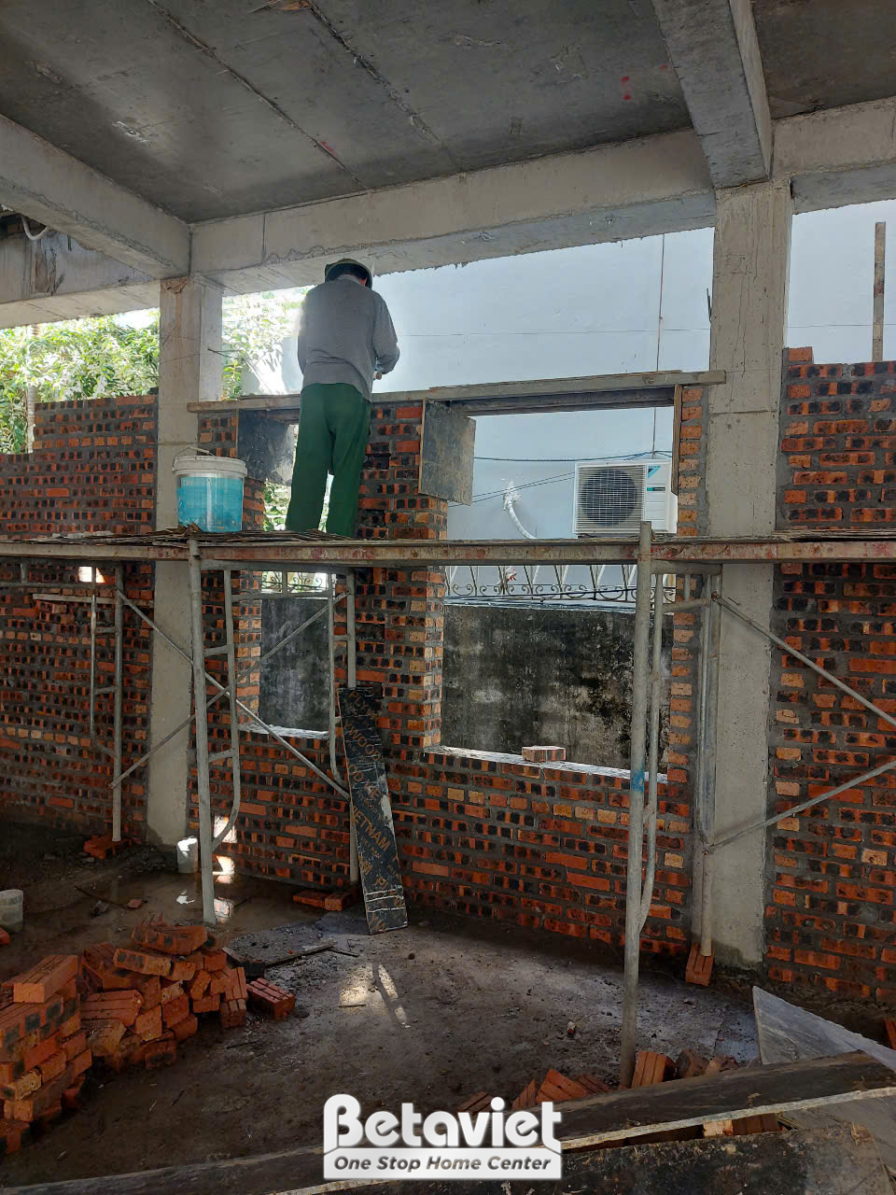 Công nhân đang thực hiện công việc xây tường gạch bên trong ngôi nhà phố. Giàn giáo tạm được dựng lên, ánh sáng tự nhiên c…
