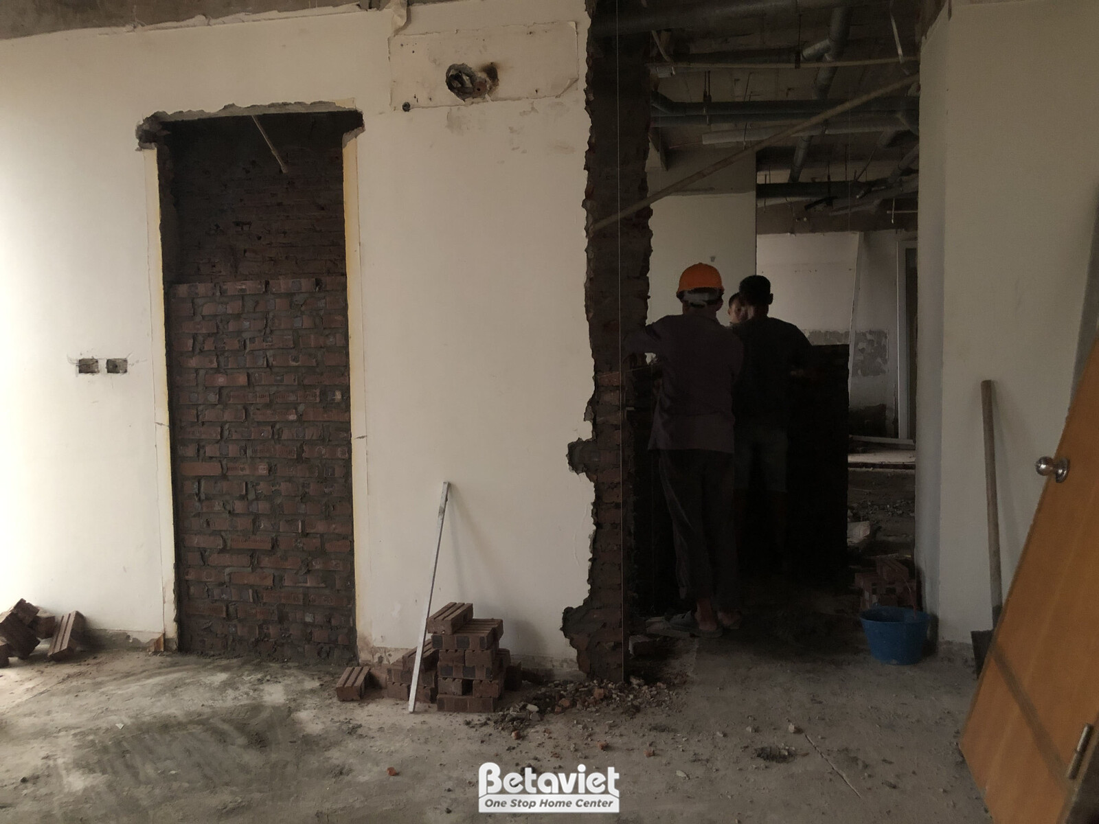 Công nhân đang xây dựng một mảng tường gạch mới, bên cạnh là cột bê tông chịu lực. Bố cục cận cảnh, tập trung vào quá trìn…