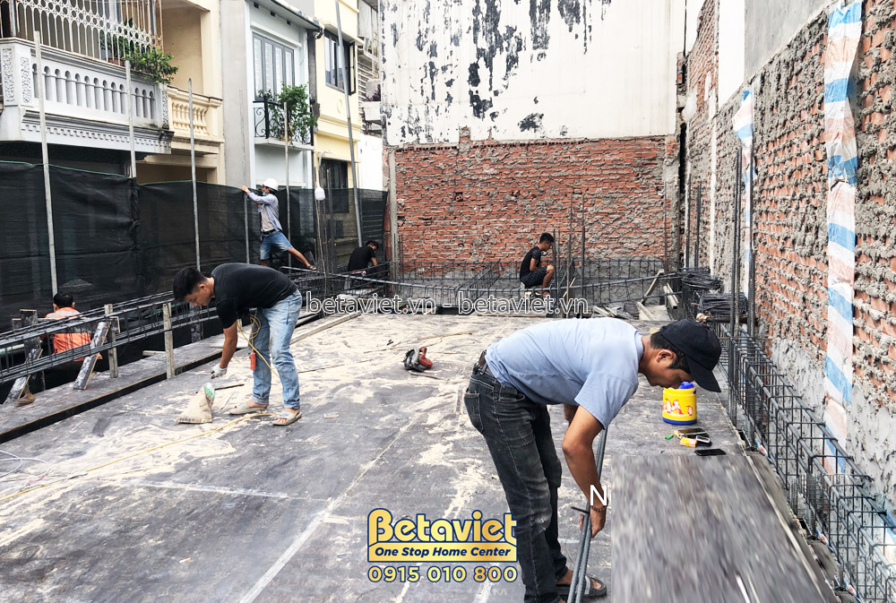 Công nhân đang chuẩn bị cốt thép và ván khuôn để đổ bê tông sàn tầng 3. Ánh sáng tự nhiên ban ngày chiếu rọi, cho thấy sự…