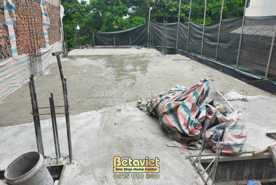 Sàn bê tông đã đổ, với các vật liệu xây dựng và dụng cụ thi công được đặt trên đó. Có lưới bảo hộ màu đen xung quanh, đảm…