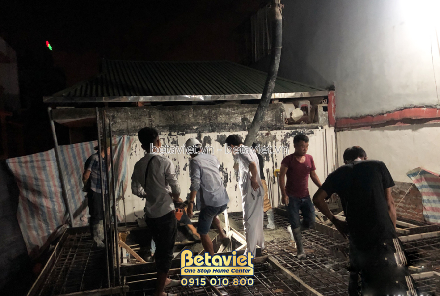 Công nhân đang đổ bê tông sàn tầng 3 vào ban đêm, với hệ thống cốt thép đã được chuẩn bị sẵn. Ánh sáng từ đèn chiếu sáng c…