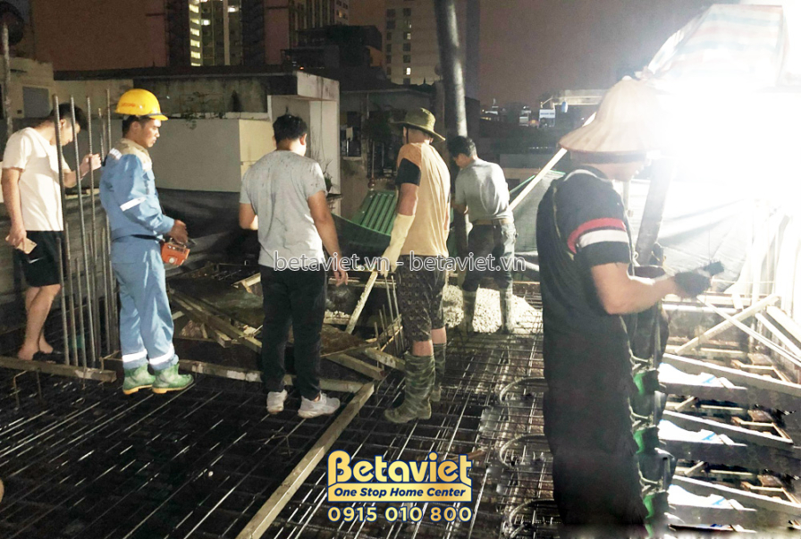 Công nhân đang chuẩn bị đổ bê tông sàn tầng 4, với hệ thống cốt thép và ván khuôn đã được lắp đặt. Ánh sáng từ đèn chiếu s…