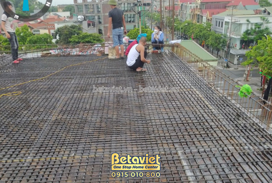 Cận cảnh sàn bê tông cốt thép đang được chuẩn bị đổ, với hệ thống lưới thép và ống dẫn. Công nhân đang kiểm tra và điều ch…