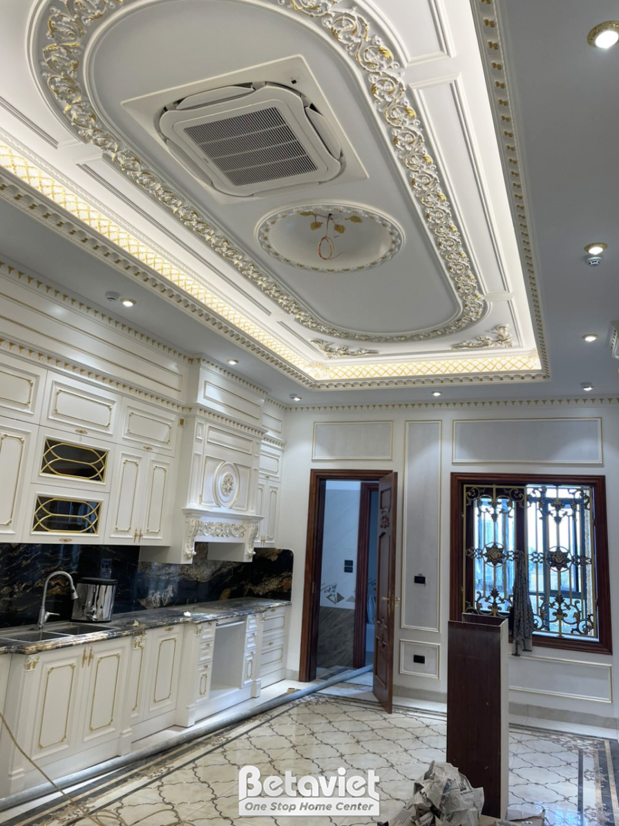 Không gian bếp hoặc khu vực ăn uống đã hoàn thiện. Hệ tủ bếp trên và dưới màu trắng kem, thiết kế tân cổ điển. Trần thạch…
