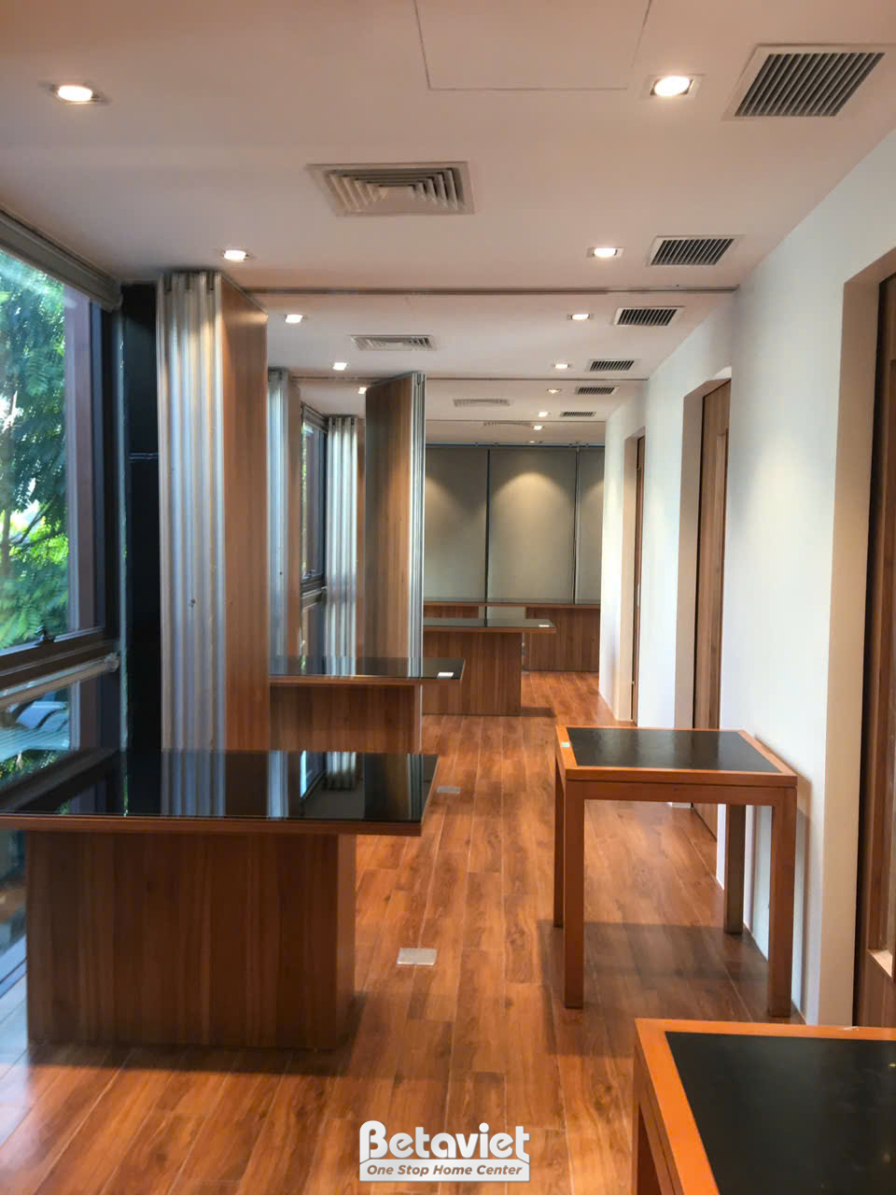 Không gian hành lang hoặc khu vực ăn uống chung, nhìn từ góc rộng. Bố cục với các bàn ăn gỗ vuông vắn, ghế bọc da màu nâu…