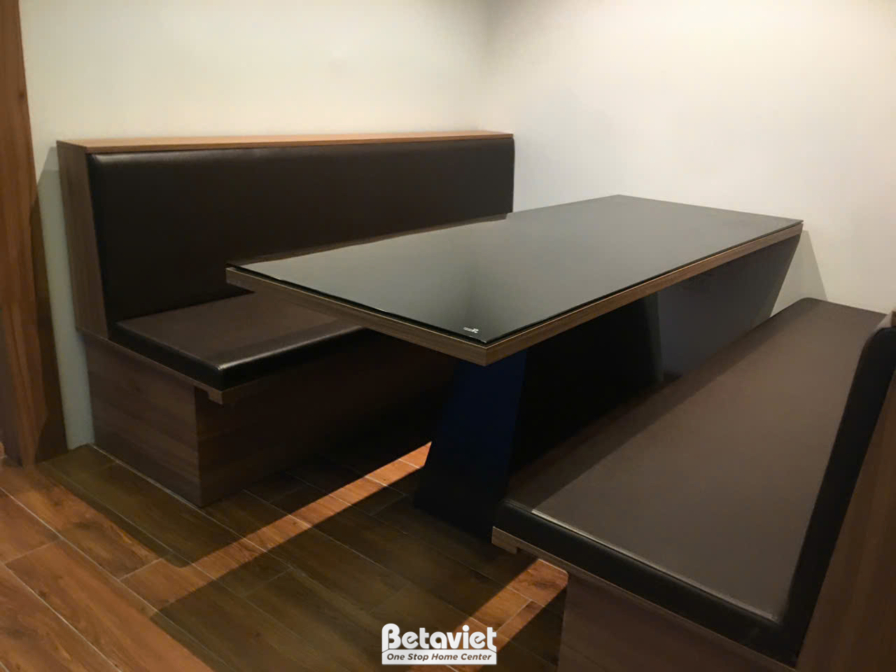 Chi tiết khu vực bàn ăn với bàn gỗ mặt kính đen, ghế sofa bọc da màu nâu đậm. Sàn nhà lát gạch giả gỗ, tạo sự đồng bộ và ấ…