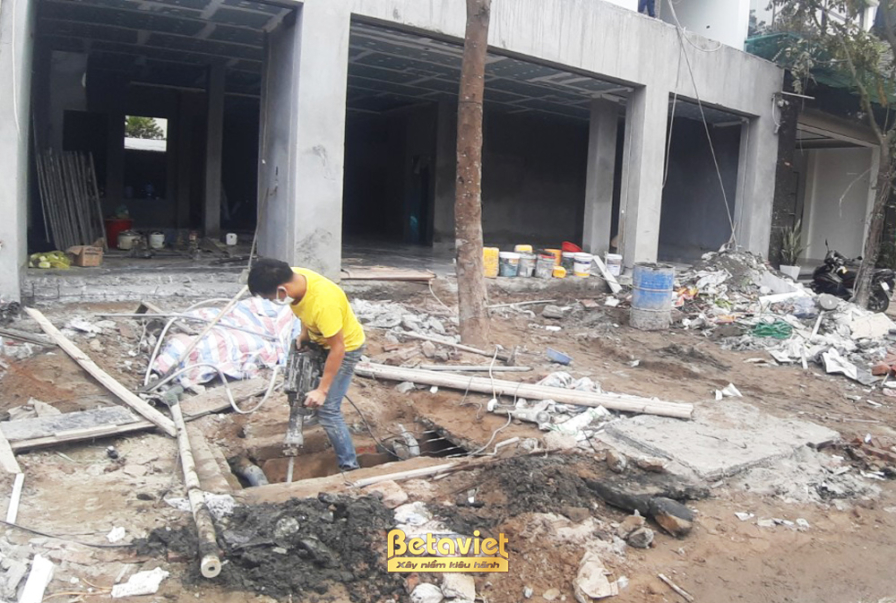Mặt tiền công trình nhà phố đang trong giai đoạn xây thô, với các bức tường gạch và hệ thống giàn giáo bao quanh. Bố cục ả…