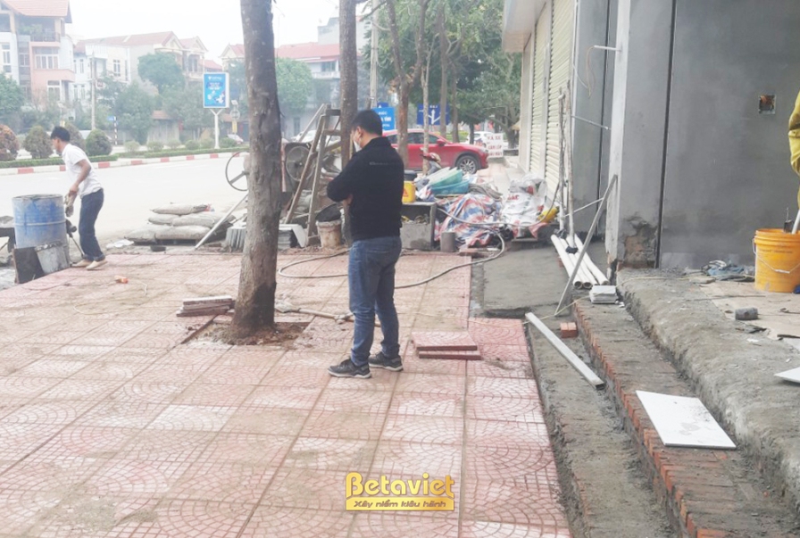 Mặt tiền công trình nhà phố đang trong giai đoạn xây thô, với các mảng tường gạch đỏ và khung cửa sổ đã định hình. Giàn gi…