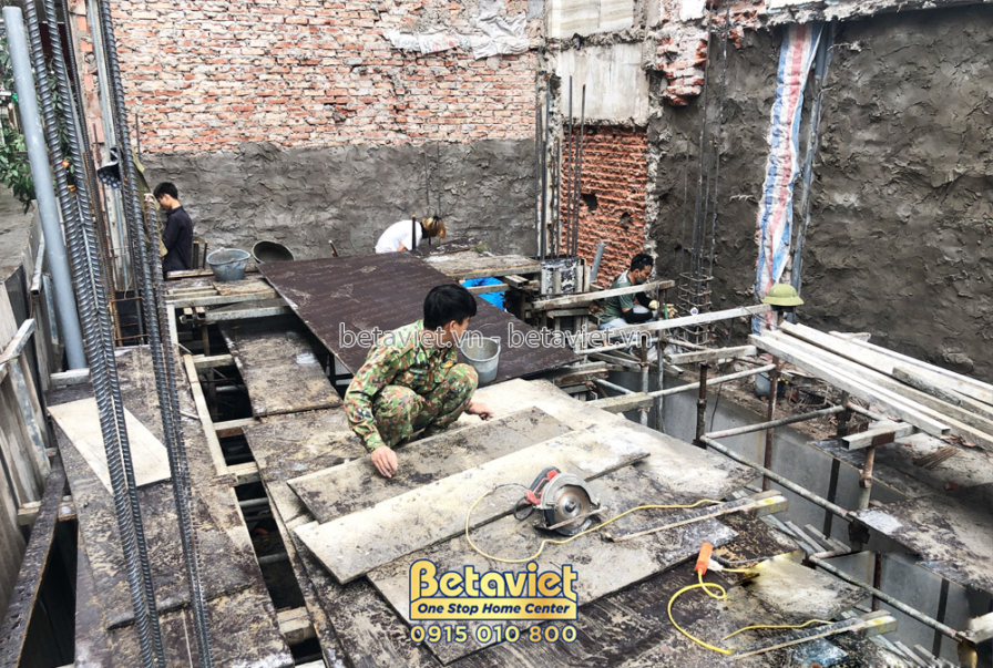 Công nhân đang chuẩn bị cốt thép và ván khuôn để đổ bê tông sàn tầng 1. Bố cục nhìn từ trên cao xuống, cho thấy tổng thể k…