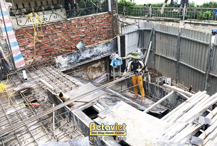 Công nhân đang chuẩn bị cốt thép và ván khuôn để đổ bê tông móng hoặc sàn tầng 1. Bố cục nhìn từ trên cao xuống, cho thấy…
