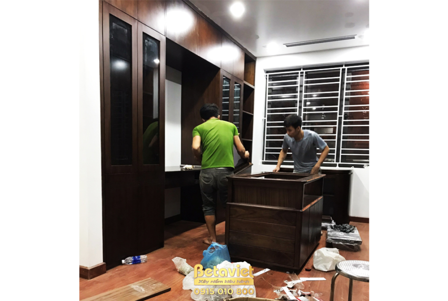 Không gian phòng ngủ với tủ quần áo gỗ công nghiệp màu nâu trầm đang được hoàn thiện. Hệ tủ quần áo lớn với các ngăn kệ mở…