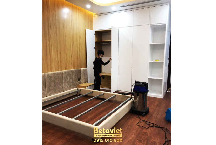 Phòng ngủ đang trong giai đoạn lắp đặt giường bục thấp và tủ quần áo âm tường cánh phẳng màu trắng. Vách đầu giường bọc nệ…