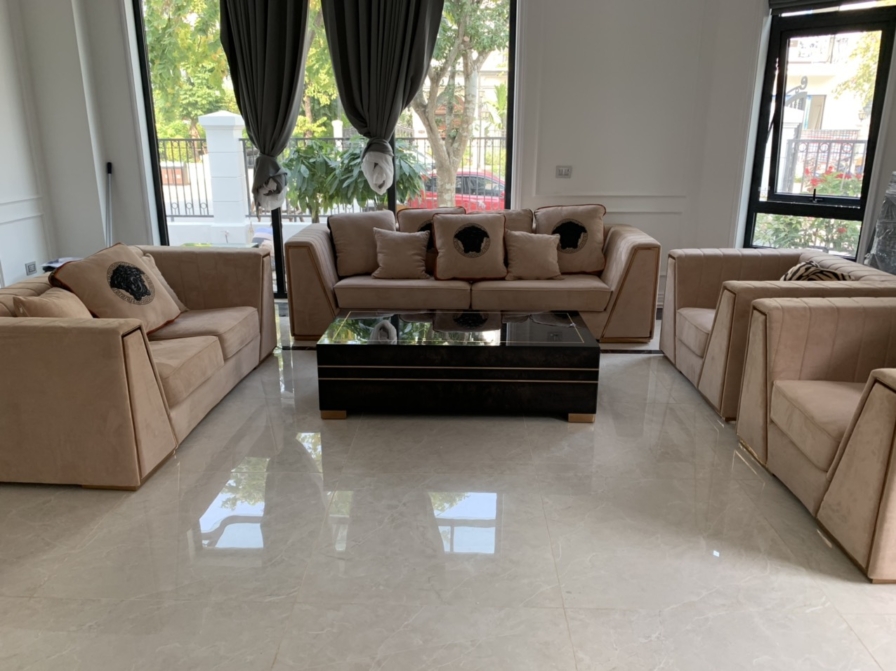 Toàn cảnh phòng khách với bộ sofa nỉ màu kem, bàn trà kính đen đặt giữa. Hệ cửa kính lớn kết hợp rèm hai lớp màu xám giúp…