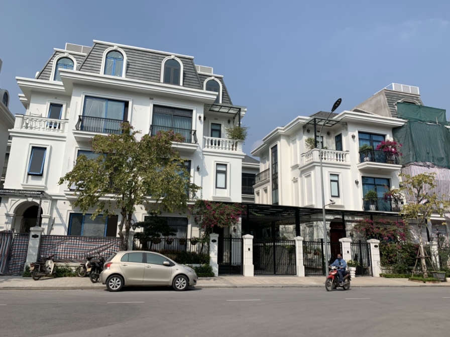 Góc nhìn tổng thể biệt thự phong cách tân cổ điển với mặt tiền trắng tinh khôi, mái mansard xám đặc trưng. Hệ cửa sổ lớn v…