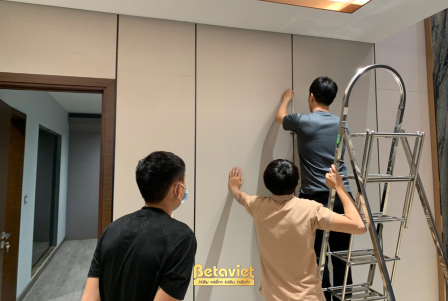 Ba kỹ thuật viên Betaviet đang cẩn thận căn chỉnh và lắp đặt các tấm ốp tường lớn màu be nhạt, tạo nên bề mặt phẳng mịn và…