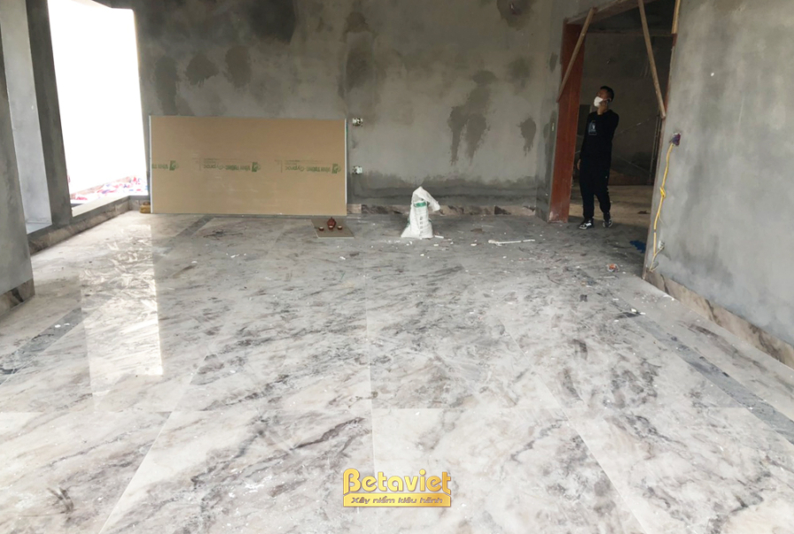 Không gian phòng đang ốp lát sàn đá vân trắng xám, tường mới trát xi măng để mộc. Tấm thạch cao dựng dựa tường chờ lắp, án…