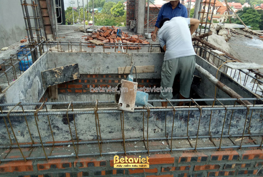 Công nhân đang xây tường gạch trên tầng mái, thể hiện tiến độ thi công phần thô của công trình nhà phố. Bố cục ảnh tập tru…