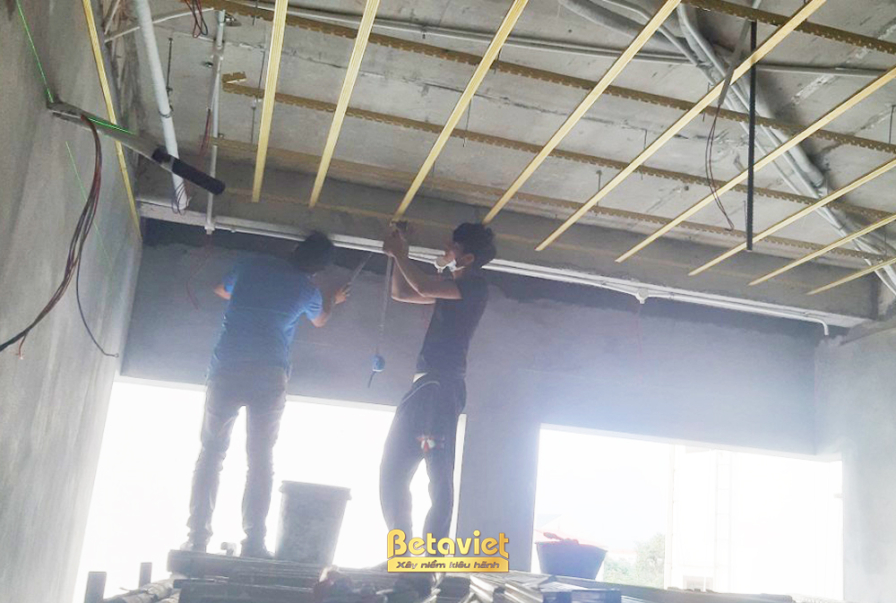 Không gian nội thất đang trong giai đoạn thi công trần thạch cao, với các công nhân đang lắp đặt khung xương và tấm thạch…