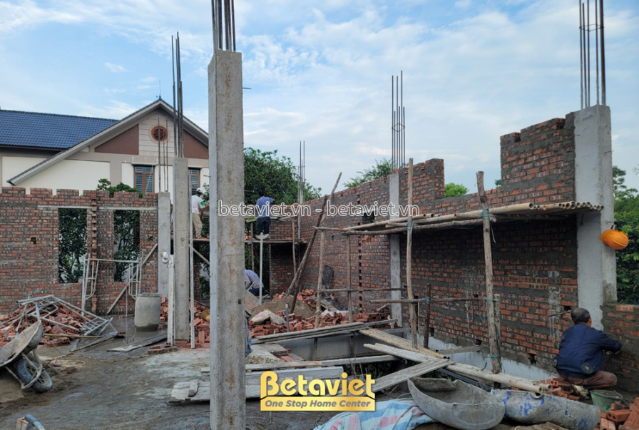 Góc nhìn từ bên trong công trình đang xây thô, với các bức tường gạch và cột bê tông đã định hình rõ ràng. Ánh sáng tự nhi…