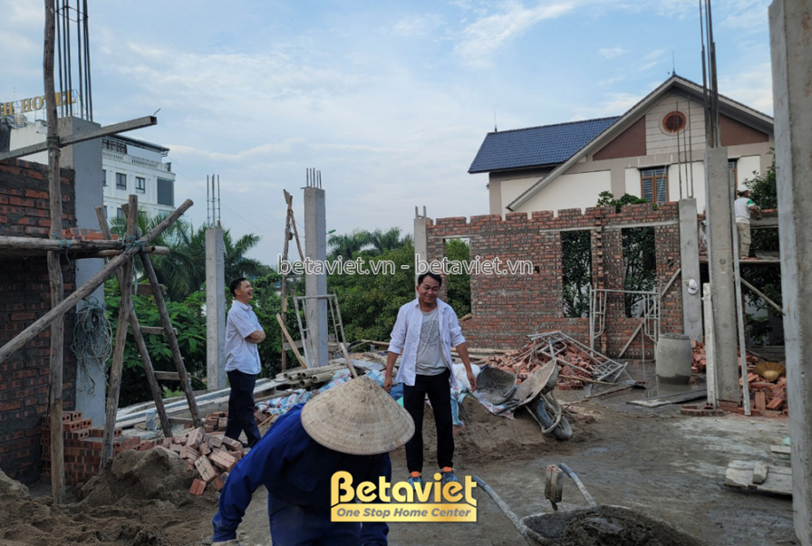 Khung cảnh công nhân đang làm việc tại khu vực tầng trệt của công trình, với các bức tường gạch đã xây cao và hệ cột bê tô…