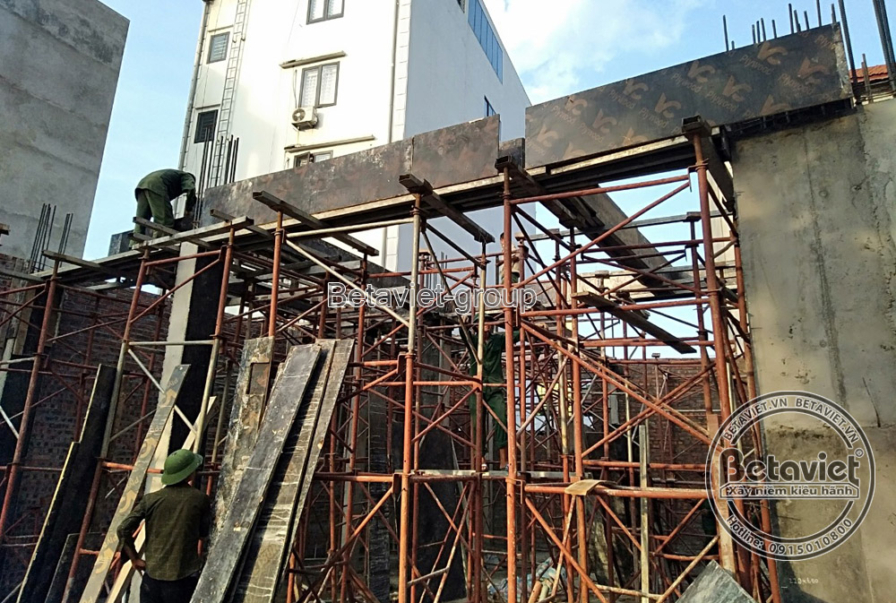 Công trình nhà phố đang trong giai đoạn xây thô, với hệ thống giàn giáo bao quanh và các cột bê tông đã được đổ. Bố cục ản…