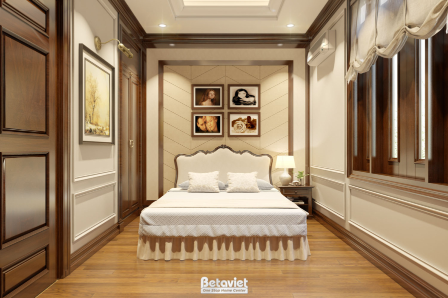 Phòng ngủ với giường gỗ đầu giường bo cong sơn trắng, ga trải màu kem, tường ốp gỗ nâu kết hợp khung ảnh treo đối xứng, sà…