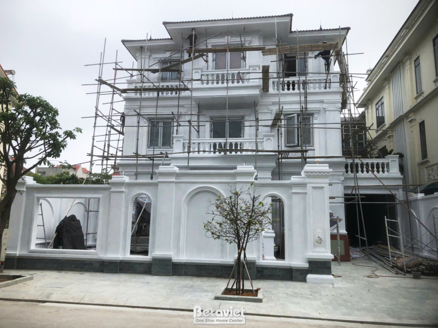 Mặt tiền ngôi nhà phố 3 tầng nhìn từ góc thấp, đang trong giai đoạn hoàn thiện ngoại thất với giàn giáo bao quanh. Các chi…