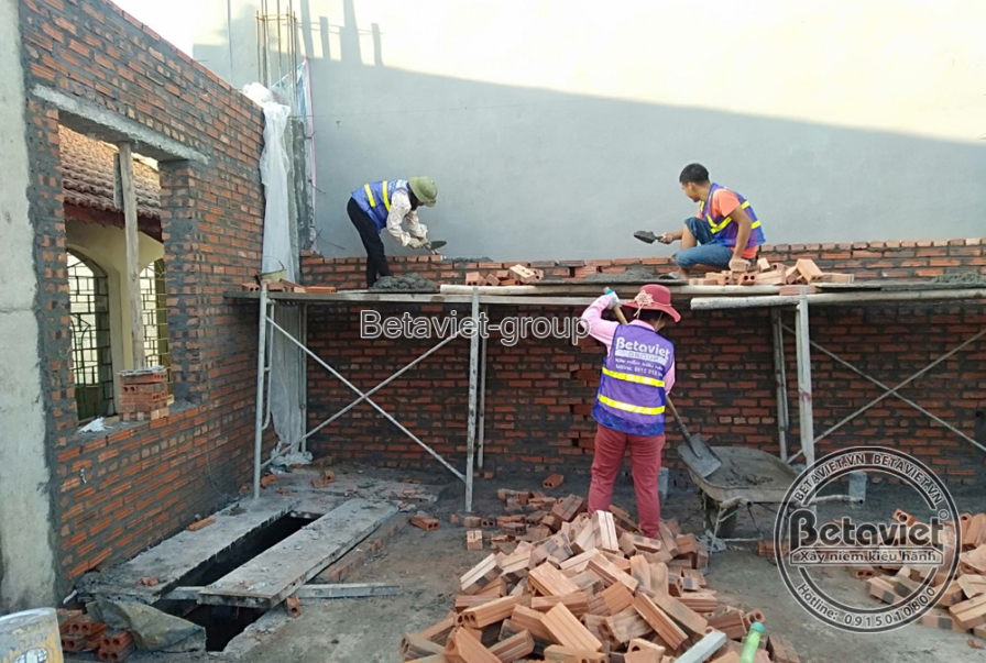 Công nhân đang xây tường gạch trên giàn giáo, thể hiện tiến độ thi công phần thô của công trình nhà phố. Bố cục ảnh tập tr…