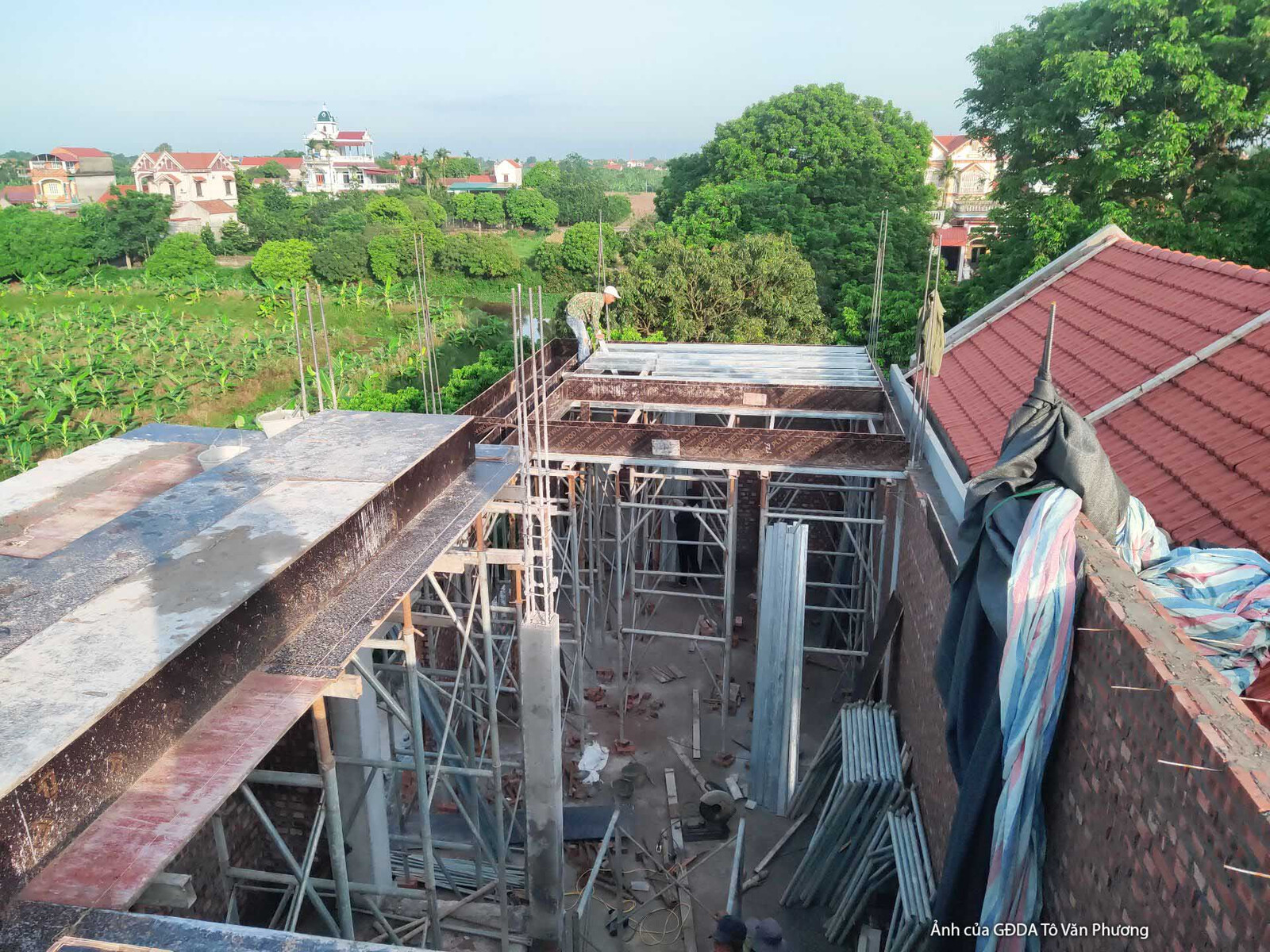 Góc nhìn từ trên cao xuống phần mái của nhà phố đang trong quá trình thi công, với hệ giàn giáo và khung thép lộ rõ. Khung…