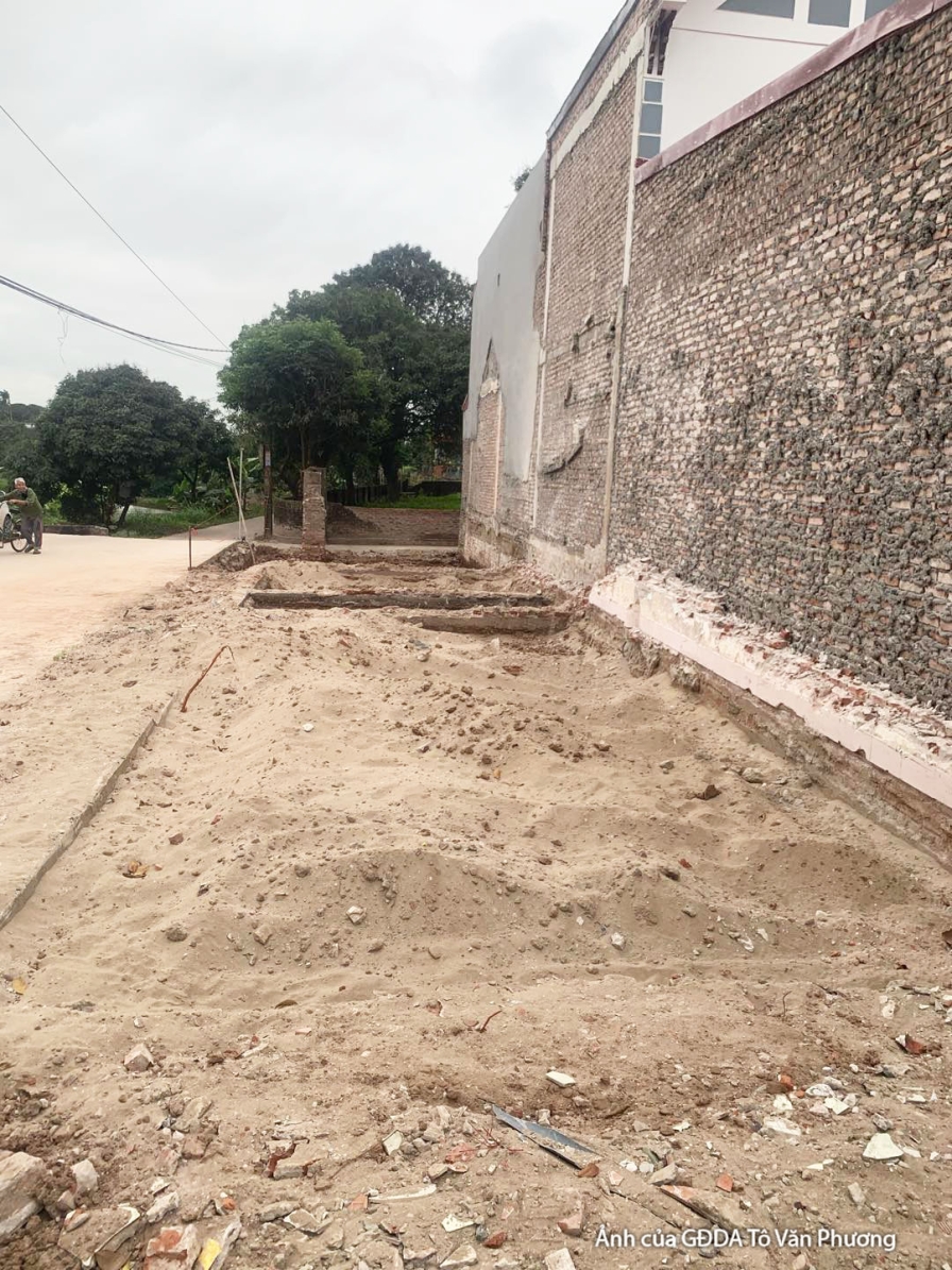 Góc nhìn ngang khu đất thi công, với mặt bằng đã được san lấp một phần và tường gạch của các công trình lân cận. Bối cảnh…
