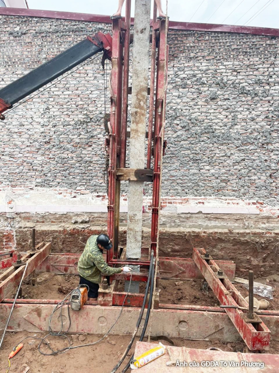 Cận cảnh hệ thống cốp pha và cốt thép đang được lắp đặt cho cột hoặc dầm, với tường gạch thô ở phía sau. Hình ảnh thể hiện…