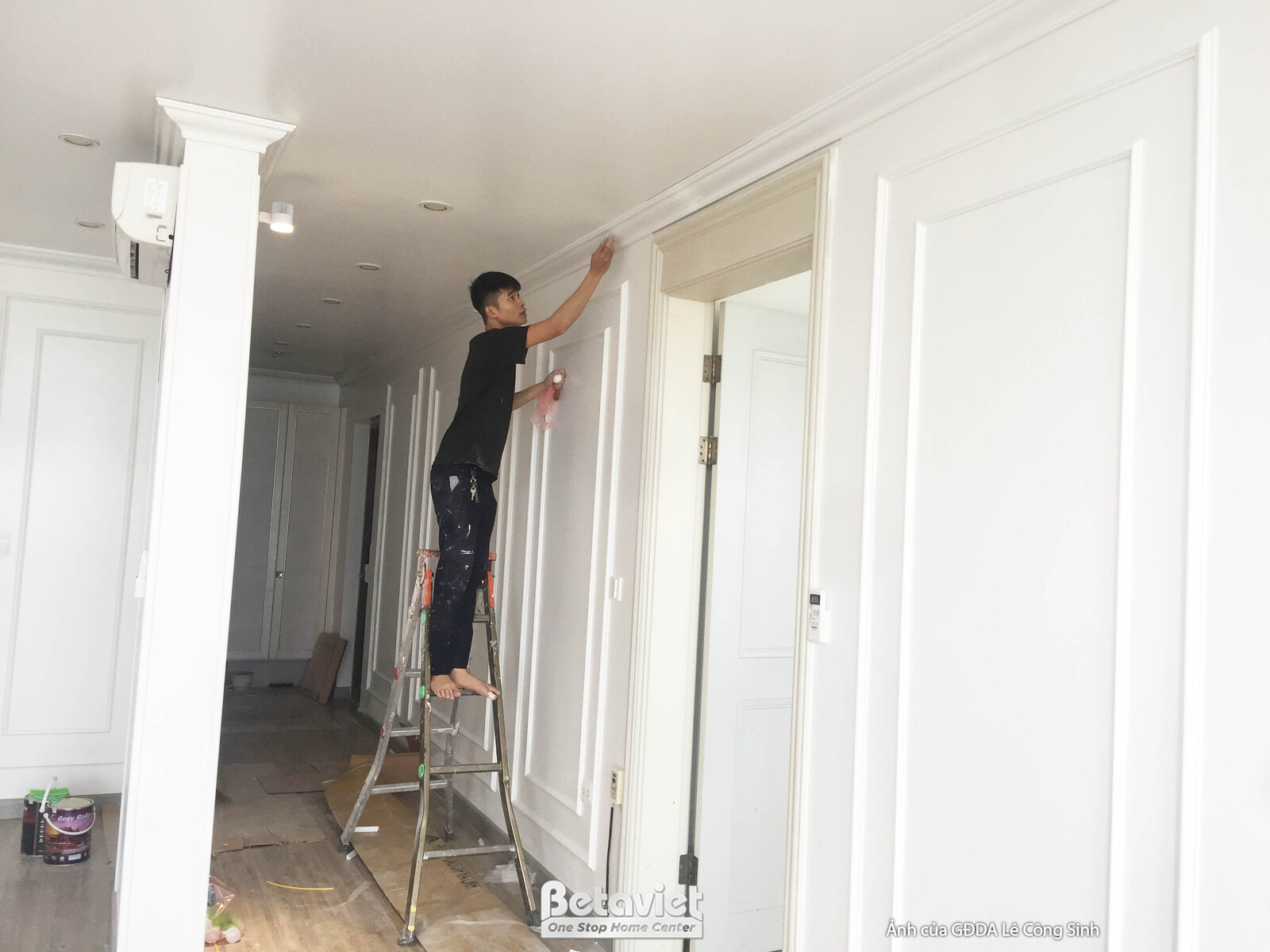 Cảnh thi công hoàn thiện chi tiết phào chỉ trên tường và trần. Một công nhân đang đứng trên thang, tỉ mỉ xử lý các đường n…
