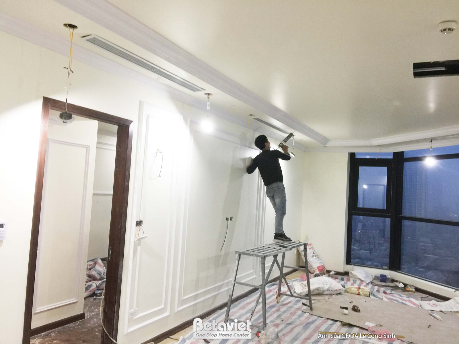 Không gian phòng khách hoặc sinh hoạt chung đang trong giai đoạn hoàn thiện cuối cùng. Một người thợ đang làm việc trên tr…