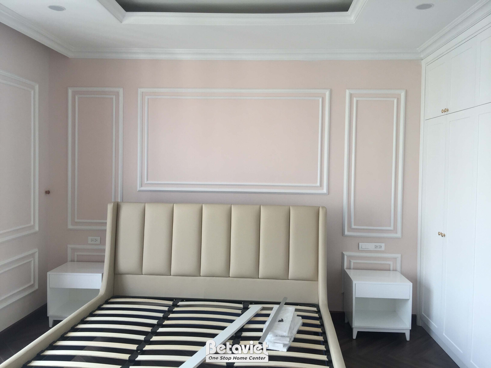 Không gian phòng ngủ đang trong giai đoạn hoàn thiện nội thất, nhìn từ góc phòng. Tường được sơn màu hồng nhạt và trang tr…