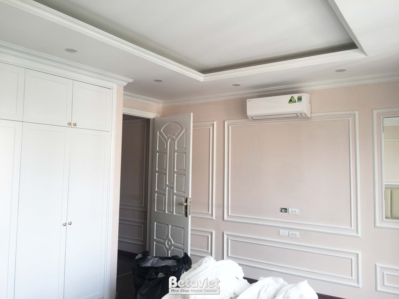 Góc phòng ngủ đang trong giai đoạn hoàn thiện nội thất, nhìn từ cửa ra vào. Tủ quần áo âm tường màu trắng với thiết kế hiệ…