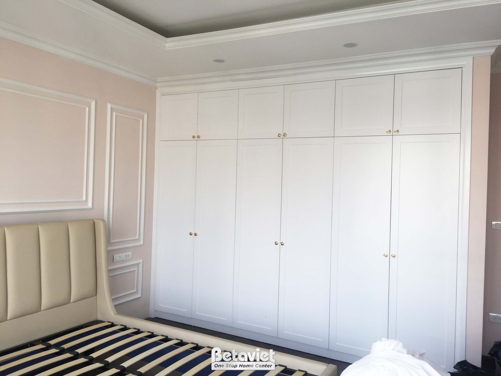 Tủ quần áo âm tường lớn màu trắng, thiết kế hiện đại với nhiều cánh tủ phẳng và tay nắm kim loại màu vàng, đã được lắp đặt…