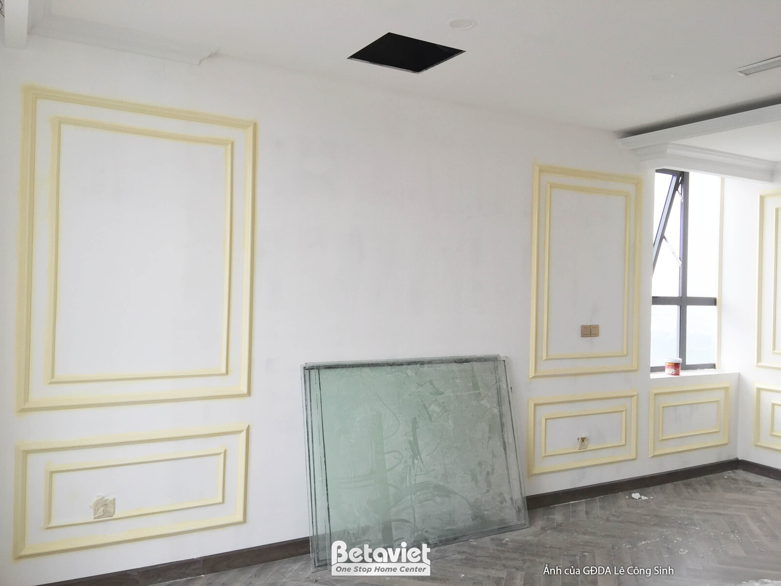 Góc phòng đang thi công nội thất với tường được trang trí phào chỉ tân cổ điển màu trắng kem và viền vàng nhạt, tạo vẻ tha…