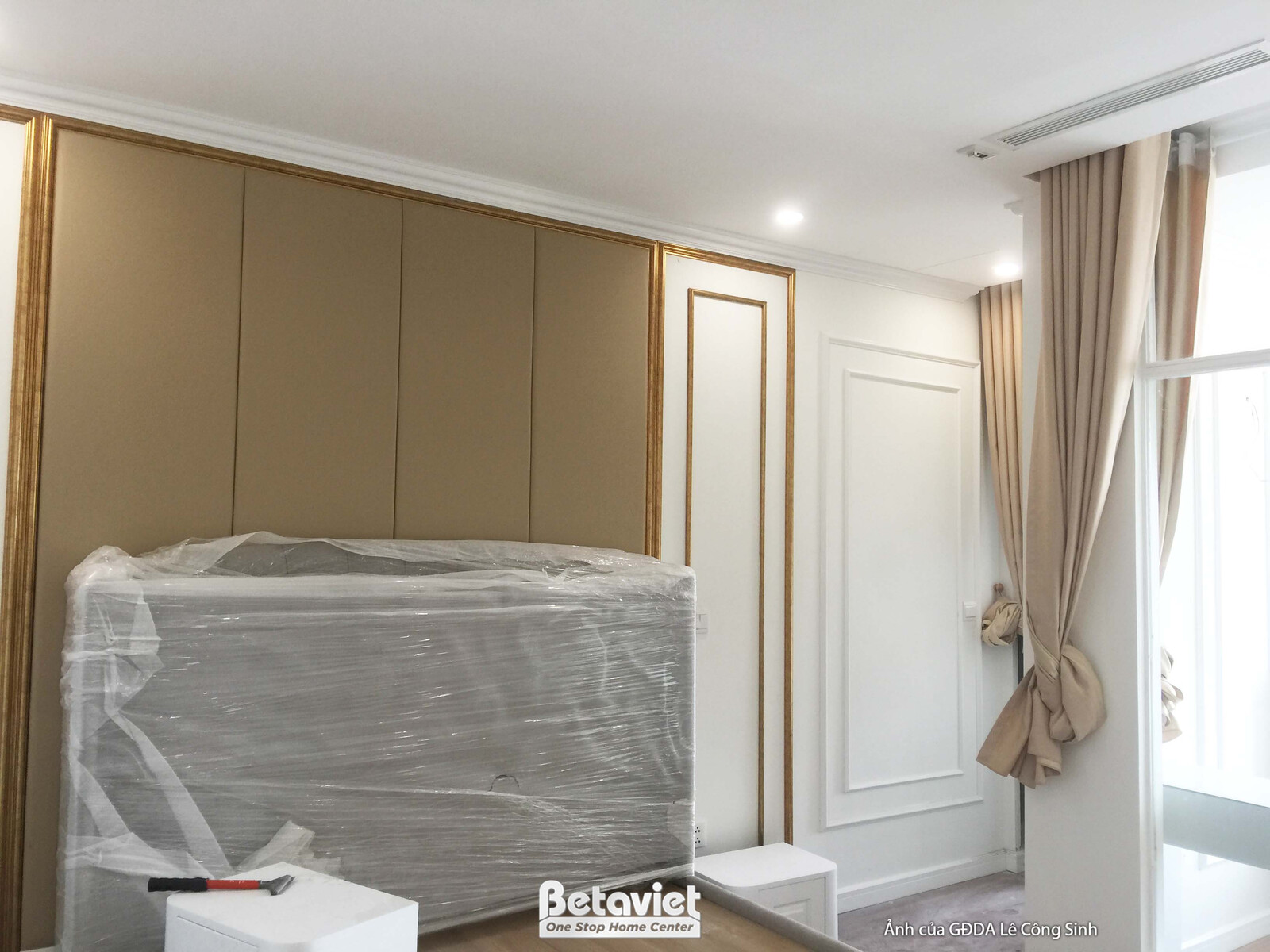 Không gian phòng ngủ hoặc phòng khách, với bức tường đầu giường hoặc tường trang trí ốp gỗ màu be/nâu nhạt kết hợp phào ch…