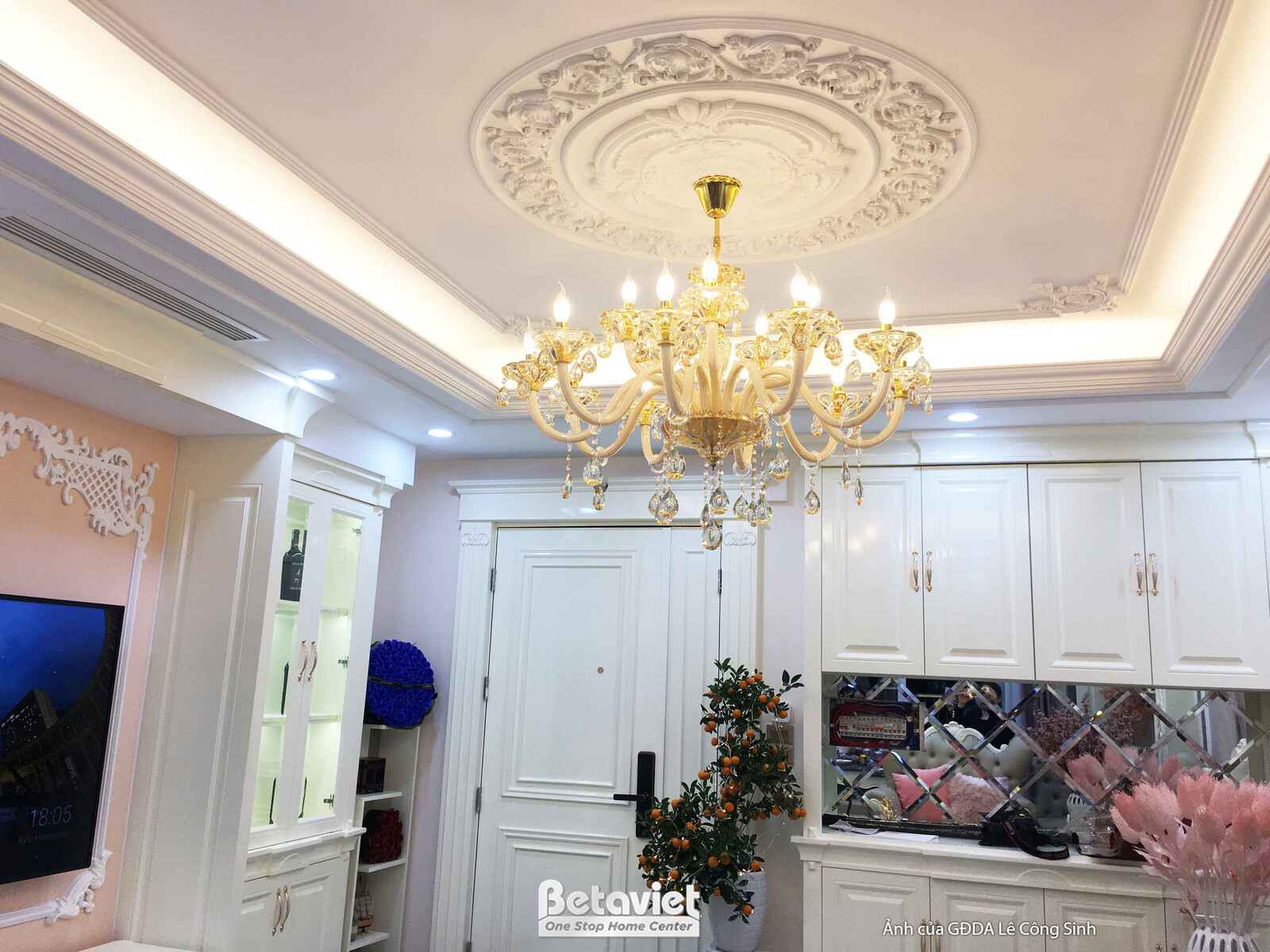Cận cảnh trần phòng khách với đèn chùm pha lê vàng lộng lẫy, trung tâm là họa tiết hoa văn thạch cao chạm khắc tinh xảo. T…