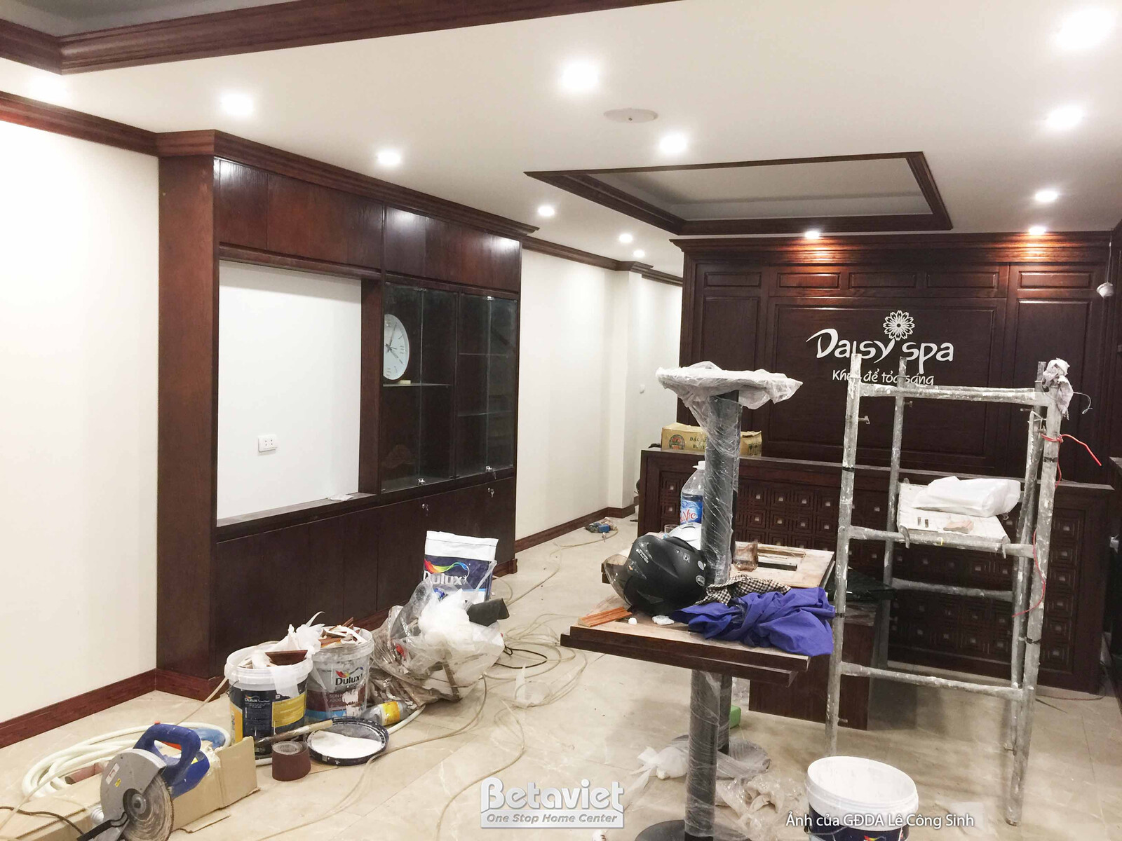 Góc nhìn rộng hơn khu vực lễ tân spa, cho thấy không gian đang được thi công với vật liệu và dụng cụ ngổn ngang. Bố cục tậ…