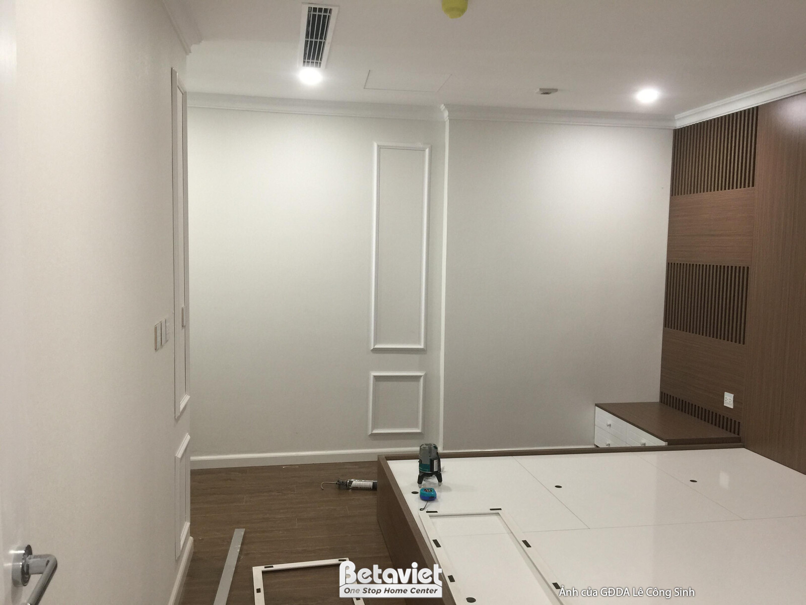 Không gian phòng ngủ hoặc phòng làm việc với mảng tường đầu giường ốp gỗ màu nâu ấm, tạo điểm nhấn sang trọng. Tường còn l…