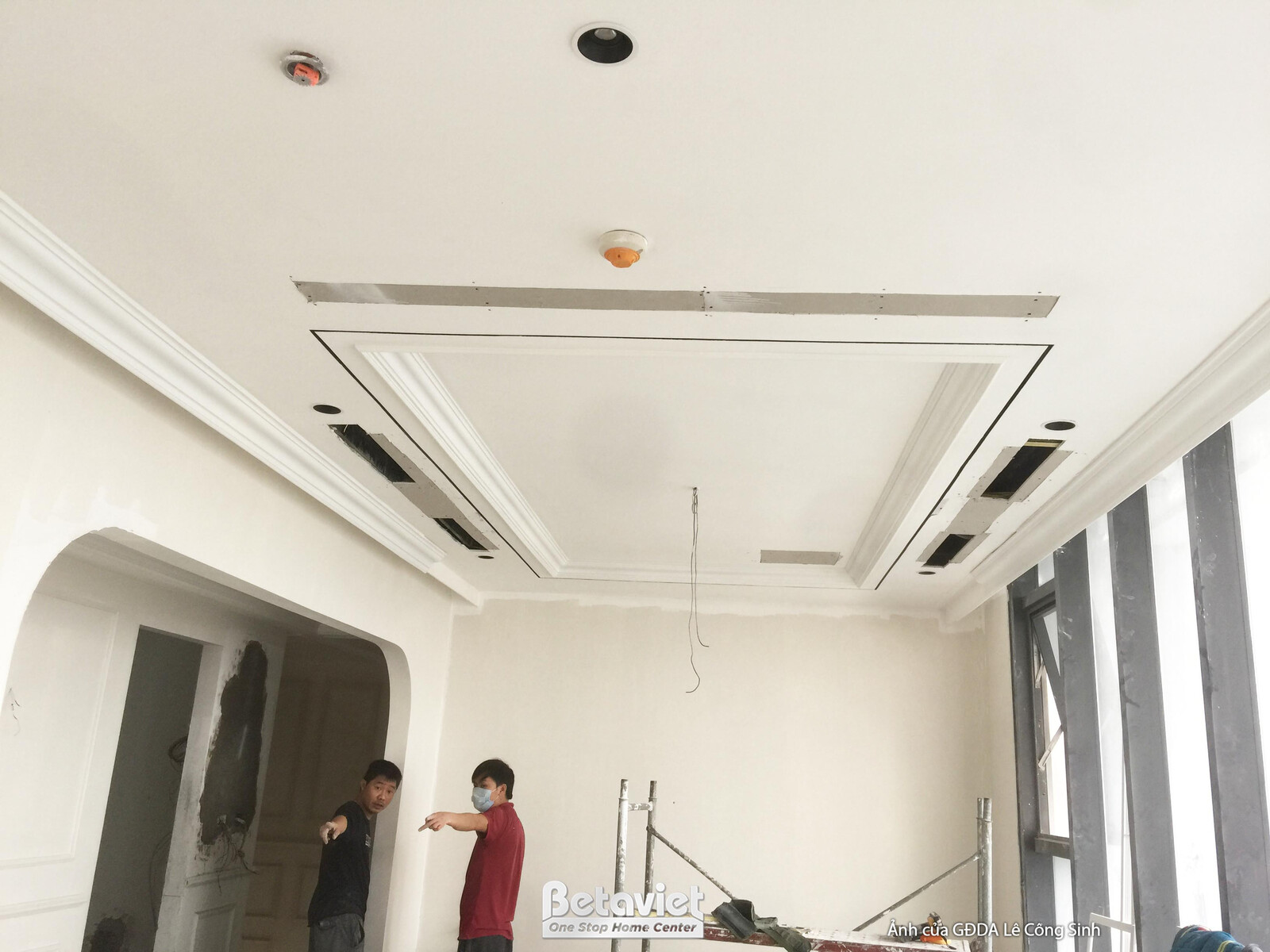 Không gian phòng khách thông tầng đang trong giai đoạn hoàn thiện trần thạch cao giật cấp với phào chỉ tinh tế. Ánh sáng t…