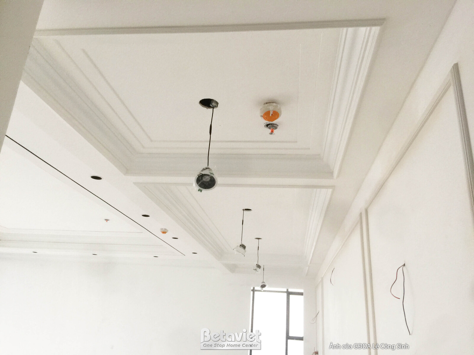 Trần thạch cao giật cấp với các đường phào chỉ và hệ thống đèn âm trần đang được lắp đặt. Bố cục đối xứng tạo điểm nhấn sa…