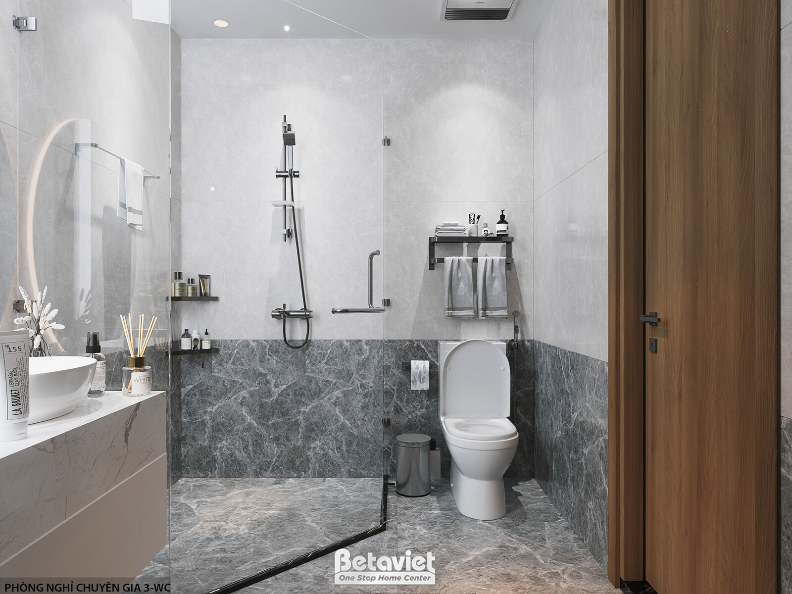 Phòng vệ sinh khu nghỉ chuyên gia với vách đá xám đậm, bồn rửa mặt đá trắng hình oval, gương tròn, vòi sen gắn tường, kệ đ…